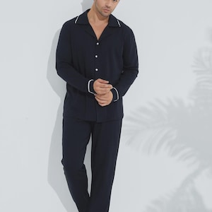 May include: Navy blue pajama set. The long-sleeved shirt has a collar and white trim on the collar and cuffs. The matching pants complete the sleepwear ensemble. The outfit is made of a soft, comfortable material.