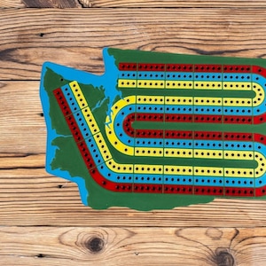 May include: A green wooden game board shaped like the state of Washington with a blue, red, and yellow track.