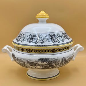 Puede incluir: Sopera de cerámica blanca con tapa y asas. La sopera presenta una escena pastoral en blanco y negro alrededor de la base y diseños florales en la tapa. La tapa tiene un adorno y un borde amarillos.