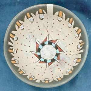 Könnte beinhalten: Eine Keramikschale mit weißem Hintergrund und einem schwarzen, roten und blauen Sternendesign in der Mitte. Die Schale hat einen grauen Rand mit einem weißen und orangefarbenen geometrischen Muster.