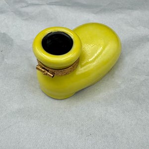Pu&ograve; includere: Un posacenere in ceramica gialla con interno nero e una fascia metallica color oro. Il posacenere ha una forma curva unica ed &egrave; posto su uno sfondo neutro.
