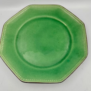 Può includere: Un piatto in ceramica ottagonale con una vivace finitura smaltata verde. Il bordo presenta una texture a perline in rilievo che segue la forma a otto lati, mentre il centro rimane liscio. I bordi del piatto mostrano una finitura marrone scuro.