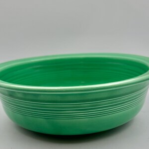 May include: A round, bright green ceramic bowl featuring a wide, flat rim and a series of concentric horizontal ridges encircling the exterior side. The bowl has a smooth, glossy finish and a deep, open interior basin with a consistent color.