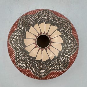 May include: A round ceramic vessel viewed from directly above, featuring a central circular opening surrounded by a cream-coloured petal pattern. The exterior surface is decorated with intricate black and red geometric line work.