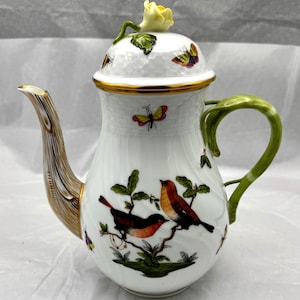 May include: White porcelain coffee pot with a lid featuring a yellow rose and butterfly details. The handle is green, and the spout has a wood-grain design. The body of the pot is decorated with birds and butterflies.