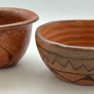 May include: Two terracotta bowls, one with a simple design and the other with a more intricate pattern of black lines and triangles.