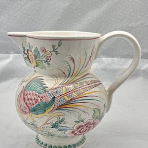 May include: Cream ceramic jug with a round body and a curved handle. The jug is decorated with a colourful peacock design, flowers, and foliage. The rim and base are trimmed with a pink and green border.