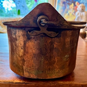 May include: A vintage copper pot with a hinged lid and a metal handle. The pot has a rustic, aged appearance with a patina of green and brown.