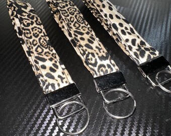 May include: Three key fobs with a leopard print design. The key fobs have a black leather loop and a silver metal ring. The leopard print pattern is tan and black.
