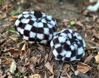 May include: Two plush pumpkin-shaped decorations featuring a black and white checkered pattern. Each soft, rounded item has a small black stem at the top, with one pumpkin noticeably larger than the other, both covered in a fuzzy, faux fur texture.