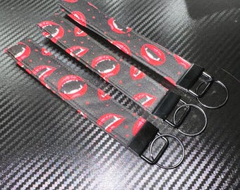 May include: Three fabric wristlet keychains featuring a repeating pattern of red vampire lips with white fangs on a black background. Each keychain includes a black metal hardware clamp and a circular silver-toned metal split ring for keys.