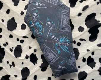 May include: A dark-colored, rectangular pillow featuring a repeating graphic of Grim Reapers with scythes, tombstones, and the letters "R.I.P." in a graveyard setting. The pillow has a black and teal color scheme.