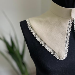 May include: A white fabric collar with a lace trim. The collar is on a black mannequin.