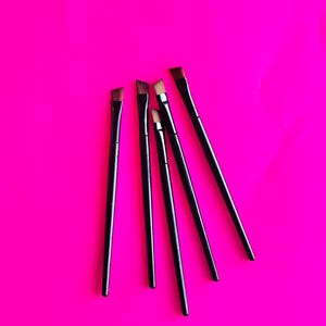 Puede incluir: Cinco pinceles de maquillaje negros con cerdas inclinadas están dispuestos sobre una superficie rosa brillante.