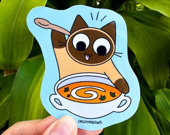 May include: A die-cut sticker depicting a cartoon Siamese cat with a spoon, eating soup from a bowl. The cat is brown and tan with large eyes and a pink tongue. The sticker includes the text "CRISPYMEOWS".