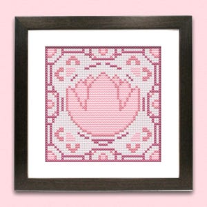 May include: A framed cross-stitch artwork featuring a pink floral design on a white background. The floral pattern is surrounded by a decorative border in shades of pink and burgundy. The frame is dark brown.