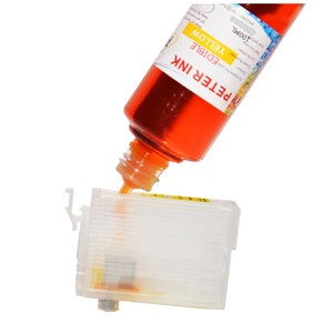 Op de afbeelding: Een transparante plastic inktcartridge wordt gevuld met gele eetbare inkt uit een fles met het label "PETER INK EDIBLE YELLOW 100ML".