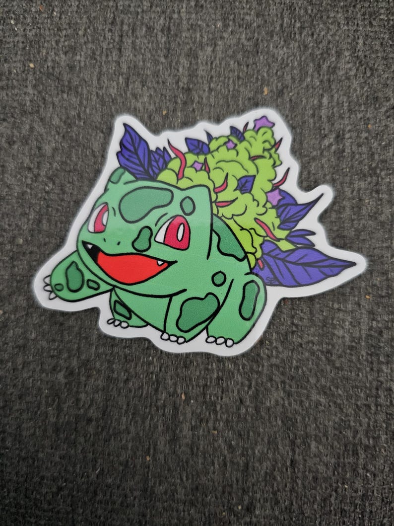 May include: A die-cut sticker featuring a green cartoon character with red eyes and a smiling red mouth. The character has green spots and is topped with a green and purple plant. The sticker is on a gray background.