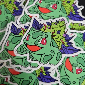 May include: A collection of stickers featuring a green cartoon character with red eyes and a smiling red mouth. The character has a green bulbous growth on its back with purple and green accents. The stickers are on a black background.