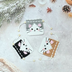 Puede incluir: Tres bolsas de cordón de ganchillo con forma de gato con diferentes colores de piel. Las bolsas están sobre una superficie gris texturizada. Las bolsas son blancas con piel gris, blancas con piel negra y blancas con piel marrón. Las bolsas tienen orejas rosas y ojos negros. El texto '@handmadify' es visible en la imagen.