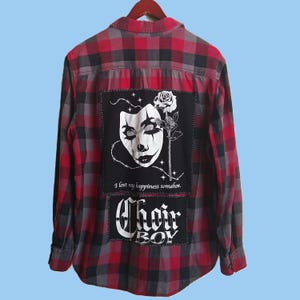 May include: Red, black, and gray plaid flannel shirt with a patch featuring a stylized face, rose, and the text "I lost my happiness somehow." Below is a patch with the text "Choir Boy."