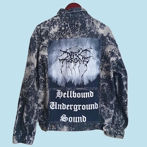 May include: A dark wash denim jacket with a bleached, distressed pattern. The back features a patch with a black and white graphic and the text "Hellbound Underground Sound."