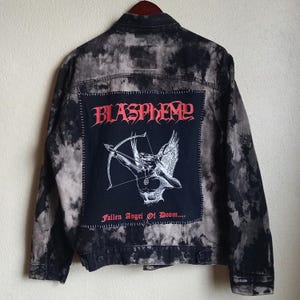 May include: A black and gray denim jacket with a large patch on the back. The patch features the word "BLASPHEME" in red gothic lettering above an illustration of an angel with a bow and arrow. The text "Fallen Angel Of Doom..." is below the illustration.