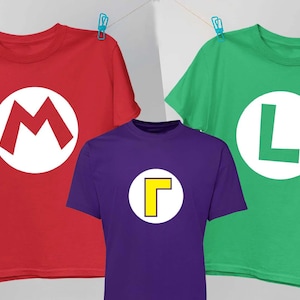May include: Three short-sleeved crew neck t-shirts hanging on a line. One is red with a white circle and a red letter M, one is green with a white circle and a green letter L, and one is purple with a white circle and a yellow letter Gamma symbol.