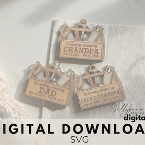 May include: Three wooden toolbox ornaments with a saw, hammer, and other tools. Each ornament has a personalized message with the text "In loving memory" and a name, followed by dates. The ornaments are on a white surface with a beige mat.