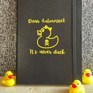 May include: A black notebook with a yellow rubber ducky graphic and the text "Dear Autocorrect It's never duck".