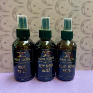 May include: Three brown glass bottles with black caps and spray tops. Each bottle is labeled with the text "Vampire Unicorns" and a different moon phase: "Moon Water", "New Moon Water", and "Blood Moon Water".