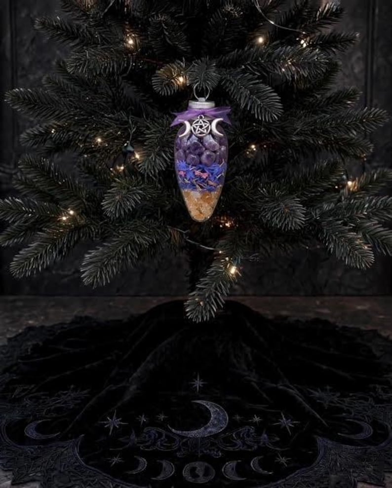 May include: A clear, teardrop-shaped glass ornament filled with layers of purple stones, blue flower petals, and yellow crystals. The top is adorned with a purple ribbon and a silver-toned metal charm featuring a pentagram and crescent moons.