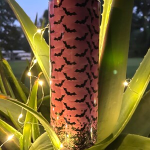 May include: A pink and black stainless steel tumbler with a bat pattern. The tumbler has a glitter finish at the bottom.