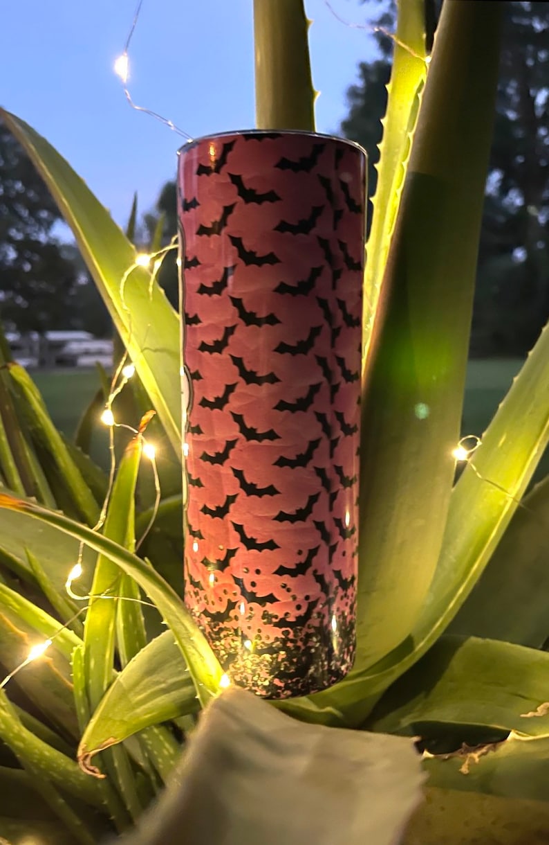 May include: A pink and black stainless steel tumbler with a bat pattern. The tumbler has a glitter finish at the bottom.