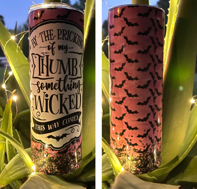 May include: A pink and black tumbler with a glittery finish. The tumbler features a white graphic with the text "By the pricking of my thumb, something wicked this way comes." and a black bat silhouette.