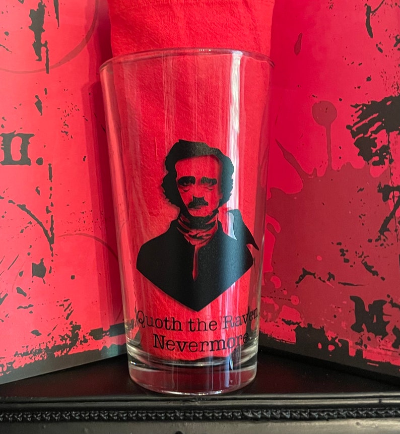 May include: A clear glass with a black silhouette of Edgar Allan Poe and a raven. The glass has the text "Quoth the Raven Nevermore" printed on the bottom.