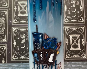 May include: A white tumbler with a blue ombre design and glitter. The tumbler features a tarot card design with a blue rose, a cup with stars, and the text "Tarot & Tea".