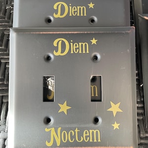 Peut inclure: Une plaque de commutateur noire avec les mots "Diem Noctem" et des étoiles en lettres dorées.