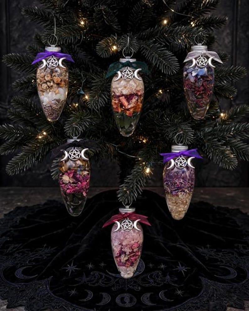 May include: Six clear, teardrop-shaped glass ornaments filled with various dried flowers, herbs, and crystals. Each ornament is topped with a silver-toned triple moon and pentagram charm, secured with a colored ribbon bow for hanging on a tree.
