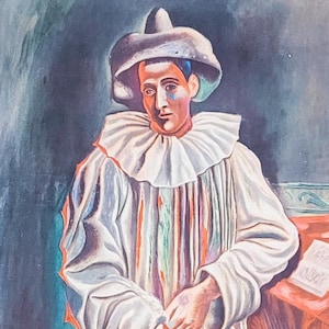 May include: A vintage print of a painting depicting a man dressed as a jester, wearing a white and red costume with a large hat. The painting is done in a cubist style with bold colors and geometric shapes.