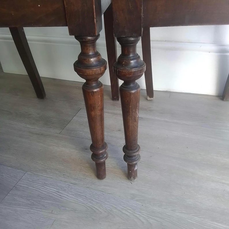 Puede incluir: Primer plano de dos patas de mesa de madera marr&oacute;n oscuro con detalles torneados. Las patas est&aacute;n unidas a una tapa de mesa, que no es visible en la imagen.
