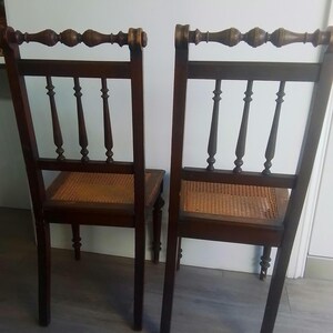 Puede incluir: Dos sillas de madera antiguas con asientos de ca&ntilde;a y  puntas decorativas en el respaldo. Las sillas son de color marr&oacute;n oscuro con un acabado desgastado.