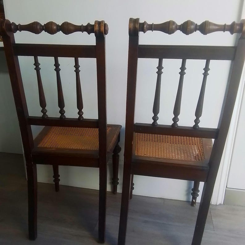 Puede incluir: Dos sillas de madera antiguas con asientos de ca&ntilde;a y  puntas decorativas en el respaldo. Las sillas son de color marr&oacute;n oscuro con un acabado desgastado.