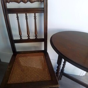 Puede incluir: Una silla de madera marr&oacute;n oscuro con un asiento de mimbre tejido y una mesa de madera marr&oacute;n oscuro a juego con una tapa redonda.