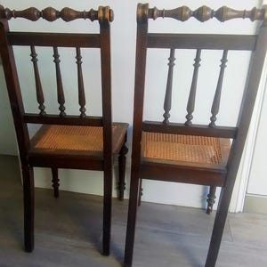 Puede incluir: Dos sillas de madera antiguas con asientos de ca&ntilde;a y patas torneadas. Las sillas tienen un acabado marr&oacute;n oscuro y detalles intrincados en el respaldo.