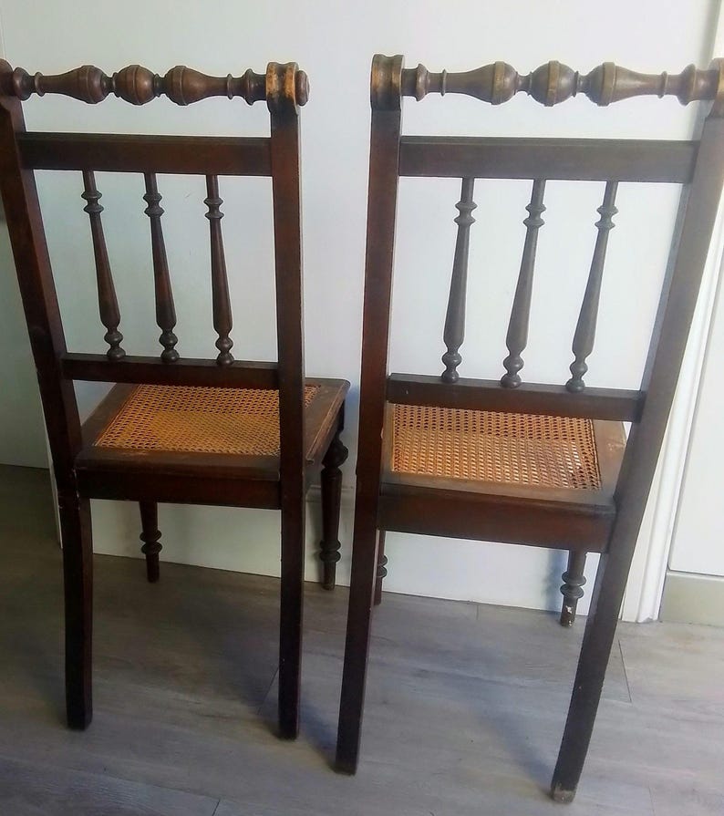 Puede incluir: Dos sillas de madera antiguas con asientos de ca&ntilde;a y patas torneadas. Las sillas tienen un acabado marr&oacute;n oscuro y detalles intrincados en el respaldo.
