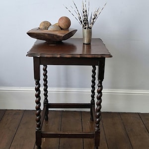 May include: A dark brown wooden side table with four barley twist legs and a scalloped edge top. On the table sits a dark wooden bowl containing several round spheres and a metallic cup filled with black and white striped porcupine quills.