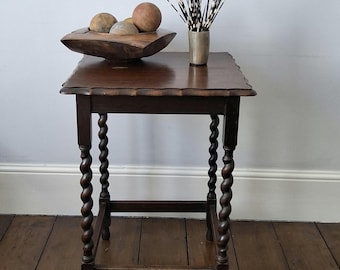 May include: A dark brown wooden side table with four barley twist legs and a scalloped edge top. On the table sits a dark wooden bowl containing several round spheres and a metallic cup filled with black and white striped porcupine quills.
