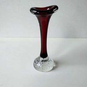 May include: A dark red glass vase with a wide, flared opening and a clear glass base with a textured bubble design.