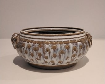 May include: A white ceramic bowl with brown speckled glaze and two small handles on the sides. The bowl has a textured surface with raised dots.